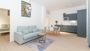 Un salon moderne avec un canapé bleu clair, un coin repas avec une table et des chaises en bois, et une cuisine avec des meubles gris et un four à micro-ondes.