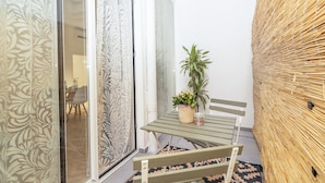Un petit espace extérieur aménagé, à l’abri, avec une table et des chaises, une plante en pot et un mur décoratif.