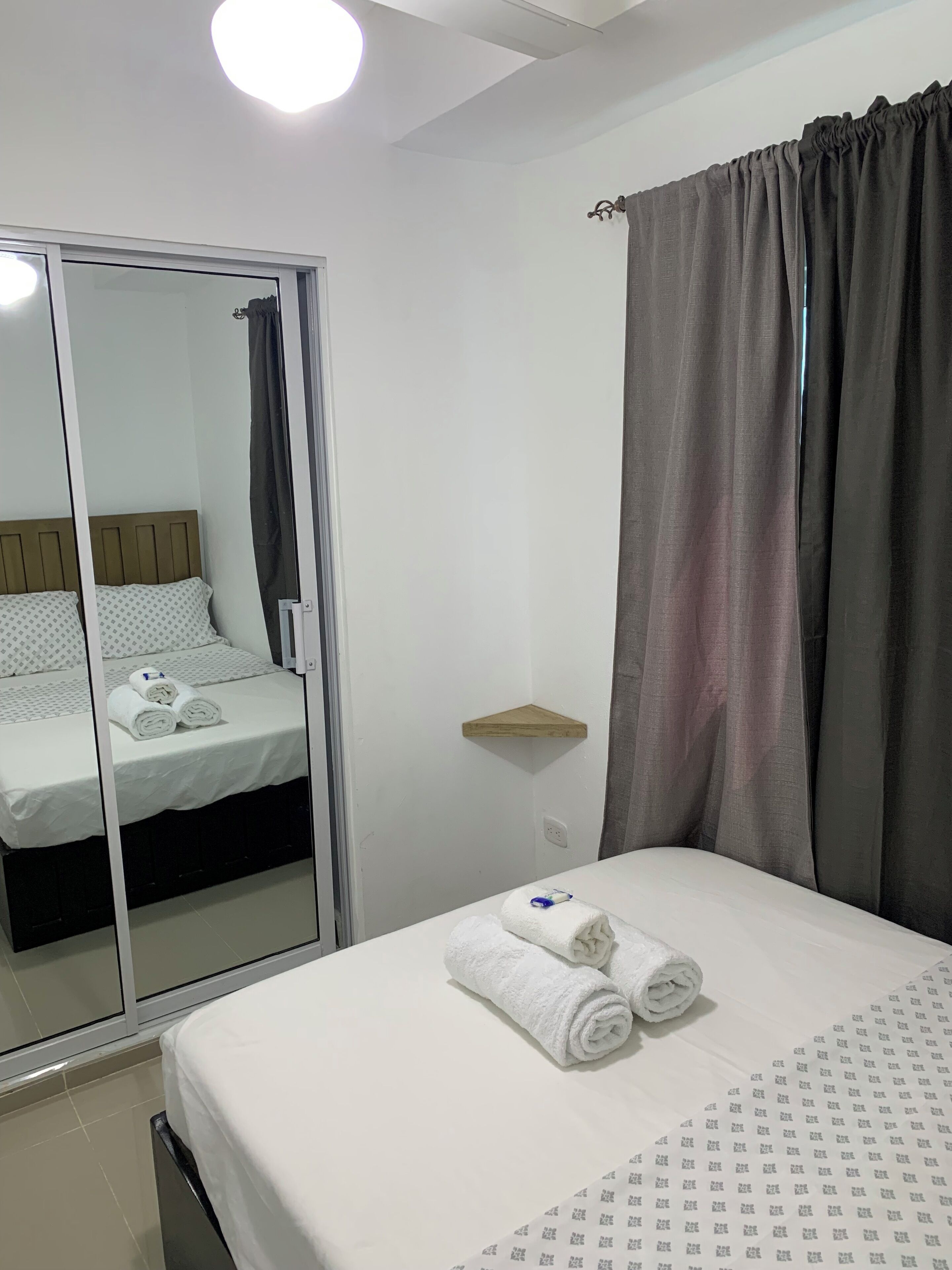 Una camera d'albergo con un letto, uno specchio, un armadio e una finestra con tende.
