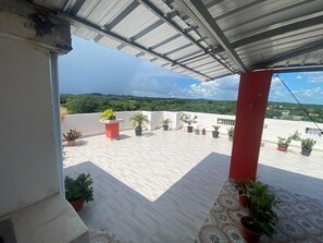 A rooftop terrace with potted plants, a red pillar, and a view of the landscape. - Plata View Apartahotel (Monte Plata)