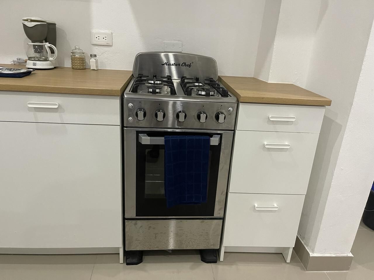Uma cozinha com fogão de aço inoxidável, cafeteira e uma toalha azul pendurada na porta do forno.