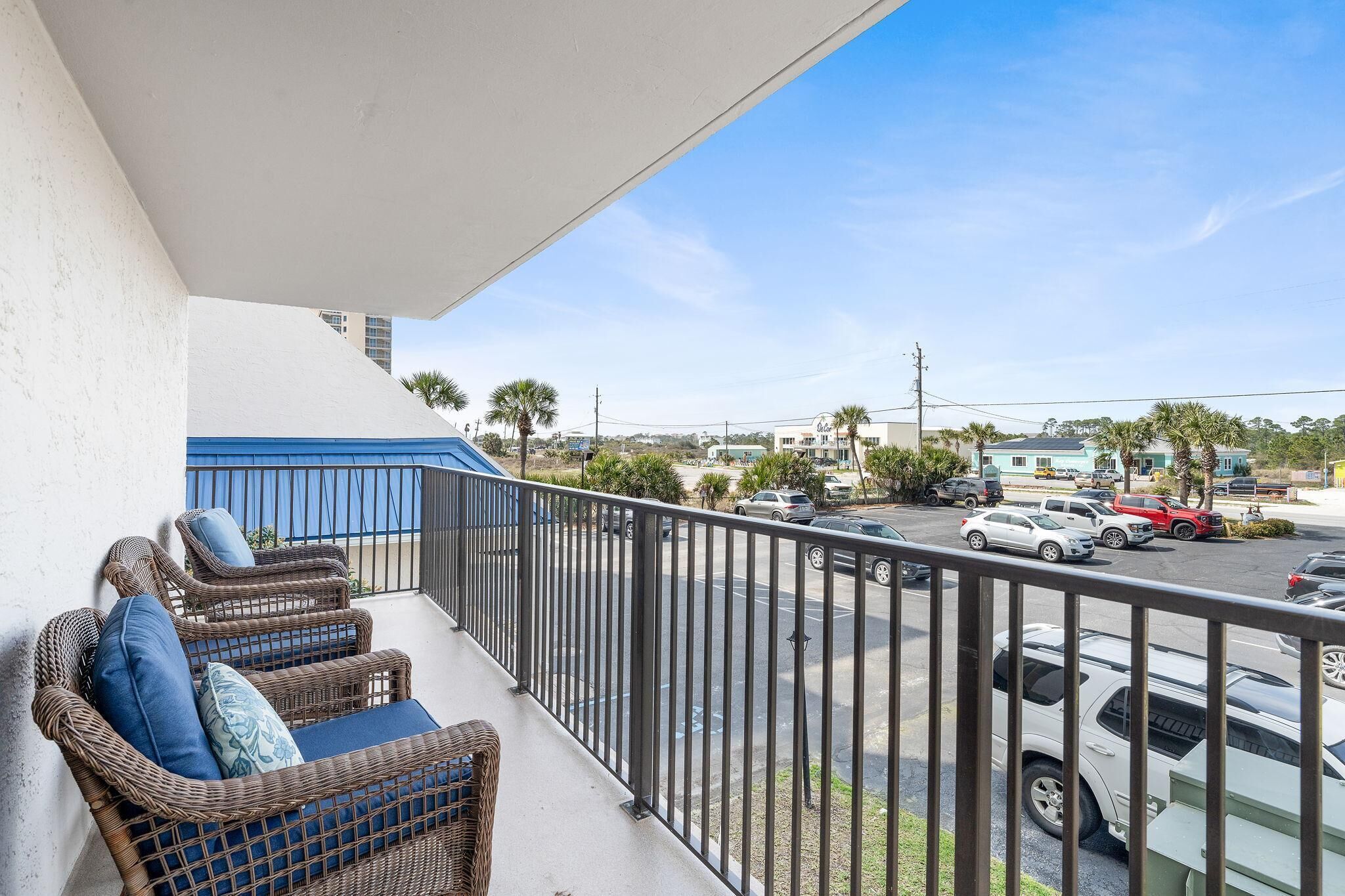 A balcony with wicker furniture and a view of a parking lot and buildings.