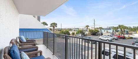 A balcony with wicker furniture and a view of a parking lot and buildings.