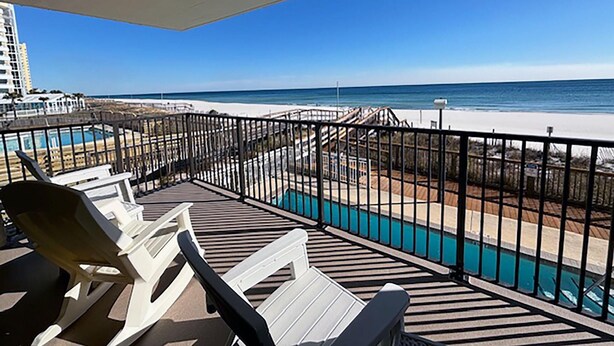 A balcony with white lounge chairs, a pool, and a view of the beach and ocean. - Ocean Breeze East 201 (Pensacola)