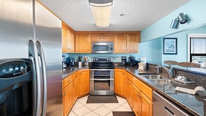 A modern kitchen with stainless steel appliances, wooden cabinets, and a granite countertop. - Ocean Breeze East 201 (Pensacola)