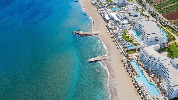 An aerial view of a coastal hotel with a long poolside, beachfront, and adjacent agricultural fields. - Kalimera studio 3 ,Near beach and all amenities (Adelianos Kampos)