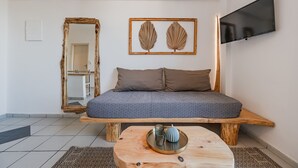 A bedroom with a bed, a wooden bench, a round coffee table, a mirror, and a framed artwork on the wall. - Kalimera studio 3 ,Near beach and all amenities (Adelianos Kampos)