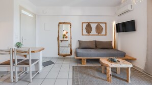 A modern living room with a sofa, a wooden coffee table, a TV mounted on the wall, and a mirror with a rustic frame. - Kalimera studio 3 ,Near beach and all amenities (Adelianos Kampos)