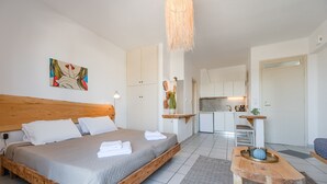A modern bedroom with a wooden bed, a small wooden table, and a kitchenette in the background. - Kalimera studio 3 ,Near beach and all amenities (Adelianos Kampos)