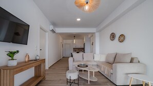 A modern living room with a large flat-screen TV, a wooden console table, a round coffee table, and a beige sofa. - Mythos villa 8,pool,Walking distance to beach (Damnoni)