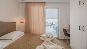 Ein Hotelzimmer mit einem Bett, einem Schreibtisch, einem Sessel und Blick durch eine Tür, sowie einer Hängelampe.