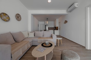 Uma sala de estar moderna com um sofá, uma mesa de centro e uma cozinha ao fundo.