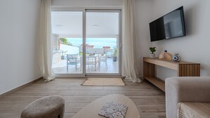 Ein modernes Wohnzimmer mit einer großen Schiebeglaswand, die zu einem Außenbereich führt, einem flachbildfernseher an der Wand und einem Holzkonsolentisch mit Dekorationen.