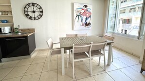 A modern kitchen with a dining table, chairs, a clock, and a window with a view of buildings.