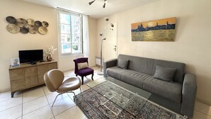 A living room with a grey sofa, a purple armchair, a glass coffee table, and a TV on a wooden cabinet.