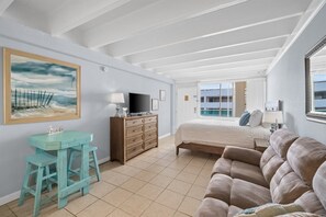 A bedroom with a bed, a dresser, a desk with a chair, a television, and a painting on the wall. - Beachfront Studio | Amazing Sunsets | Pool (Panama City Beach)