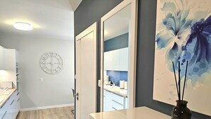 A modern kitchen with white cabinets, a clock, and a large floral artwork on the wall.