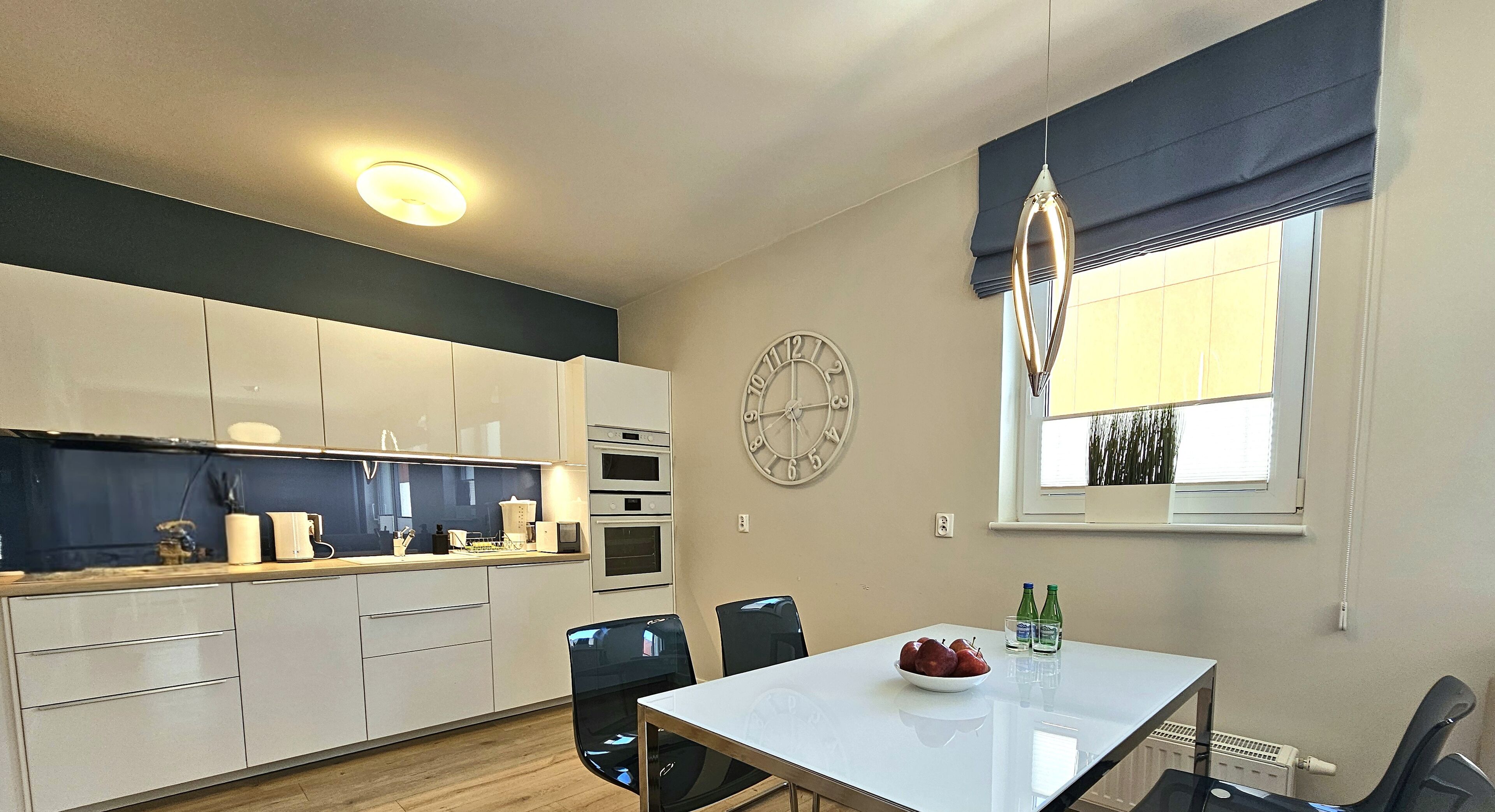 A modern kitchen with white cabinets, a dining table with chairs, and a clock on the wall.