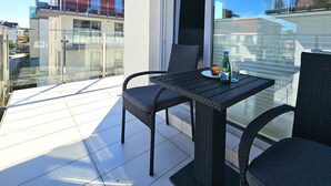 A balcony with wicker furniture, a glass table, and a bottle of water.