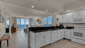 A modern kitchen with white cabinets, a black countertop, and a large island. There is a view of the ocean through the windows. - Summerwind Center 1204 (Navarre)