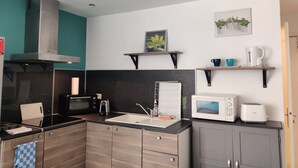 A compact kitchen with a microwave, toaster, and kettle on the countertop, a stove, and a sink. There are wooden cabinets and a teal accent wall. - Air-conditioned studio 2 min from the beach - Centre Juan-les-Pins (Antibes)