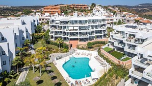 A modern resort with a central swimming pool surrounded by sun loungers and a view of the surrounding buildings.