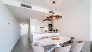 A modern kitchen with white cabinets, a central island, and a dining area with a round table and six chairs.