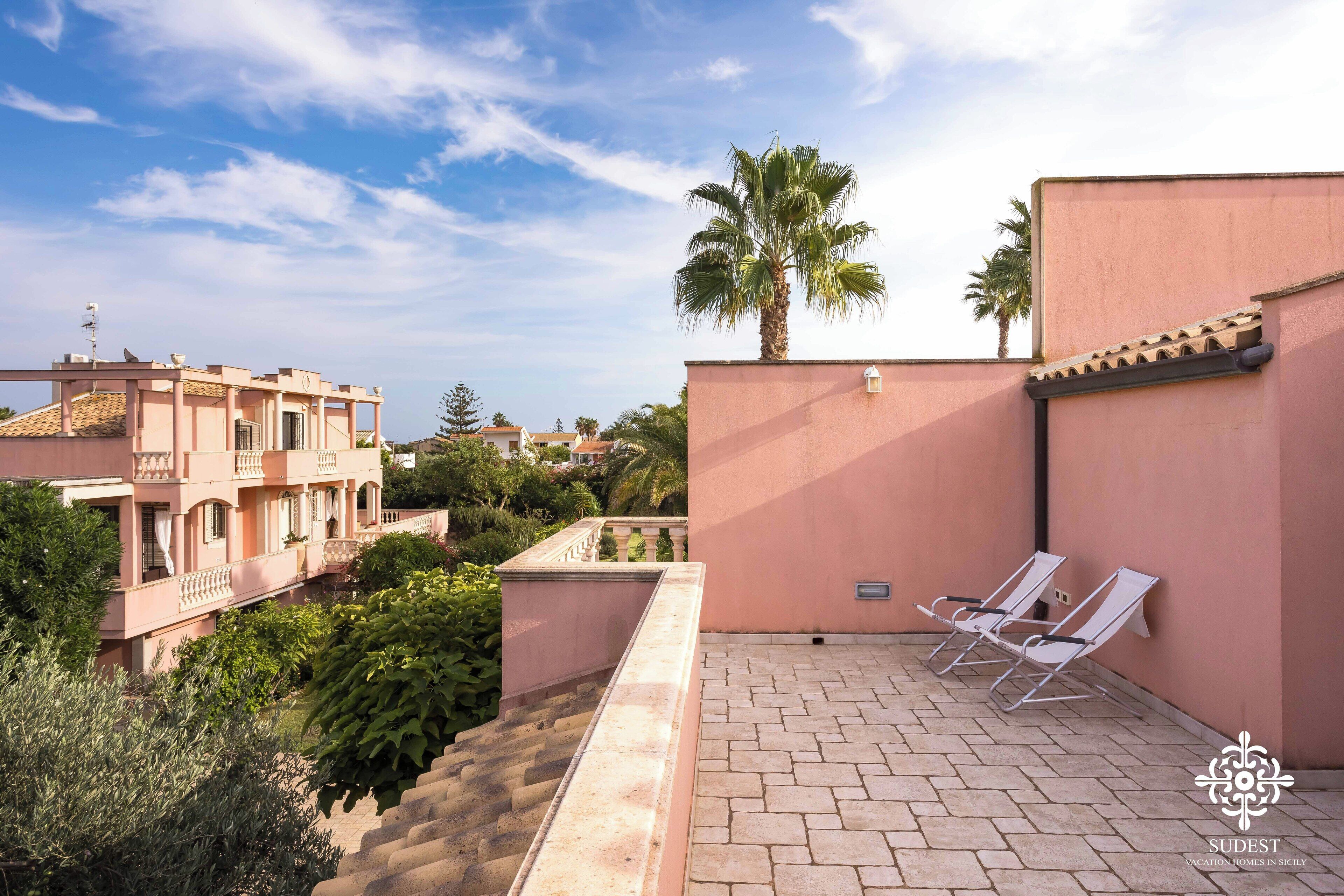 Une terrasse sur le toit, avec deux chaises longues, un palmier et une vue sur les immeubles voisins.