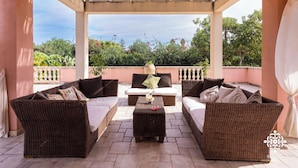 A covered outdoor seating area with wicker furniture and a view of greenery. - Villa Festosa - Luxury Retreat  (Santa Croce Camerina)