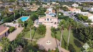 An aerial view of a residential area with a prominent pink villa featuring a swimming pool, surrounded by lush greenery and palm trees. - Villa Festosa - Luxury Retreat  (Santa Croce Camerina)