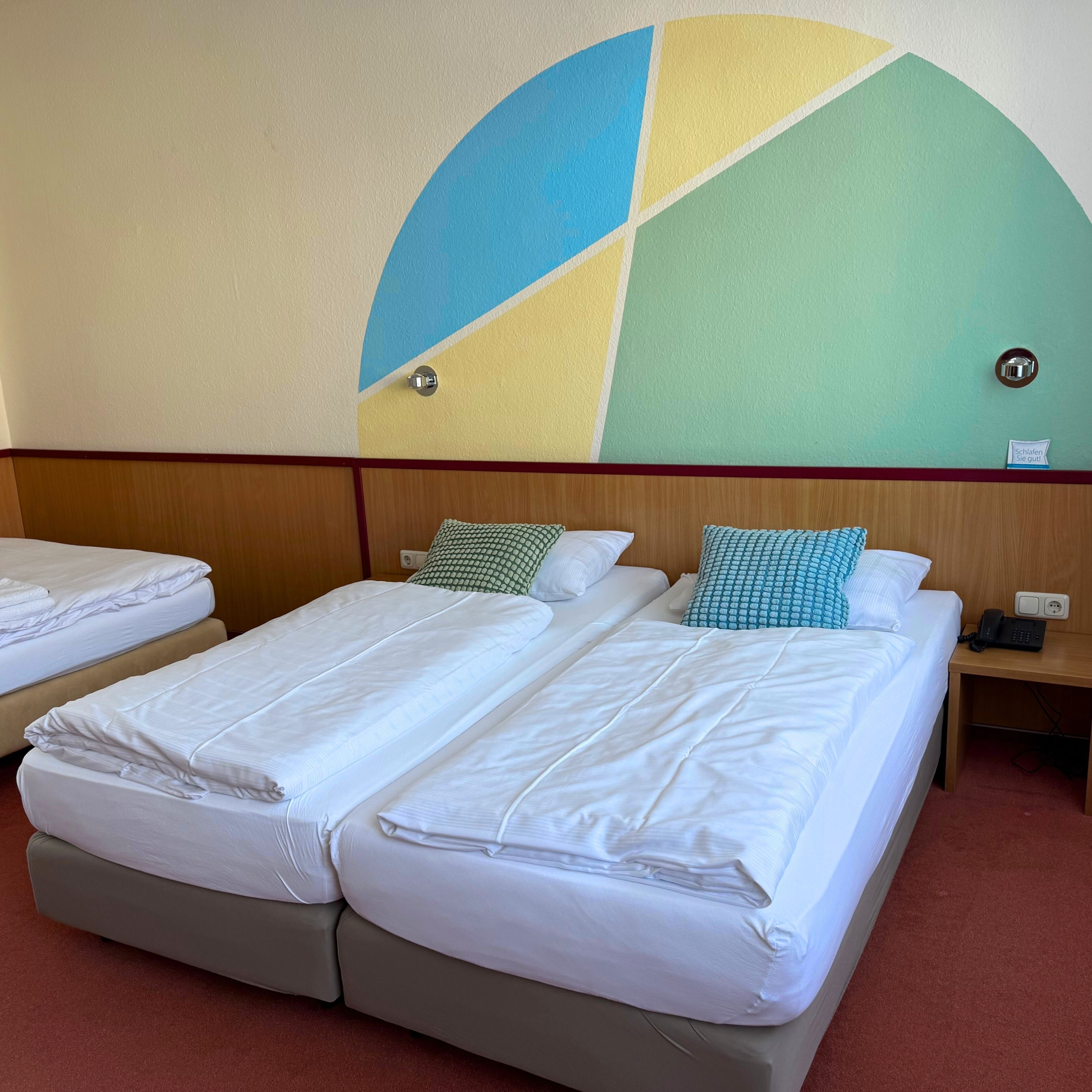 Ein Hotelzimmer mit zwei Betten, einem hölzernen Kopfteil, einer Wanduhr und einem Nachttisch mit Telefon.