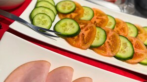 A variety of food items including sliced cucumbers and tomatoes on a white plate, with a fork on the side. - Colourful Hotel (Bielefeld)