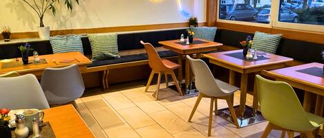 A restaurant with wooden tables and chairs, a large window with a view of the street, and a neon light design on the wall.