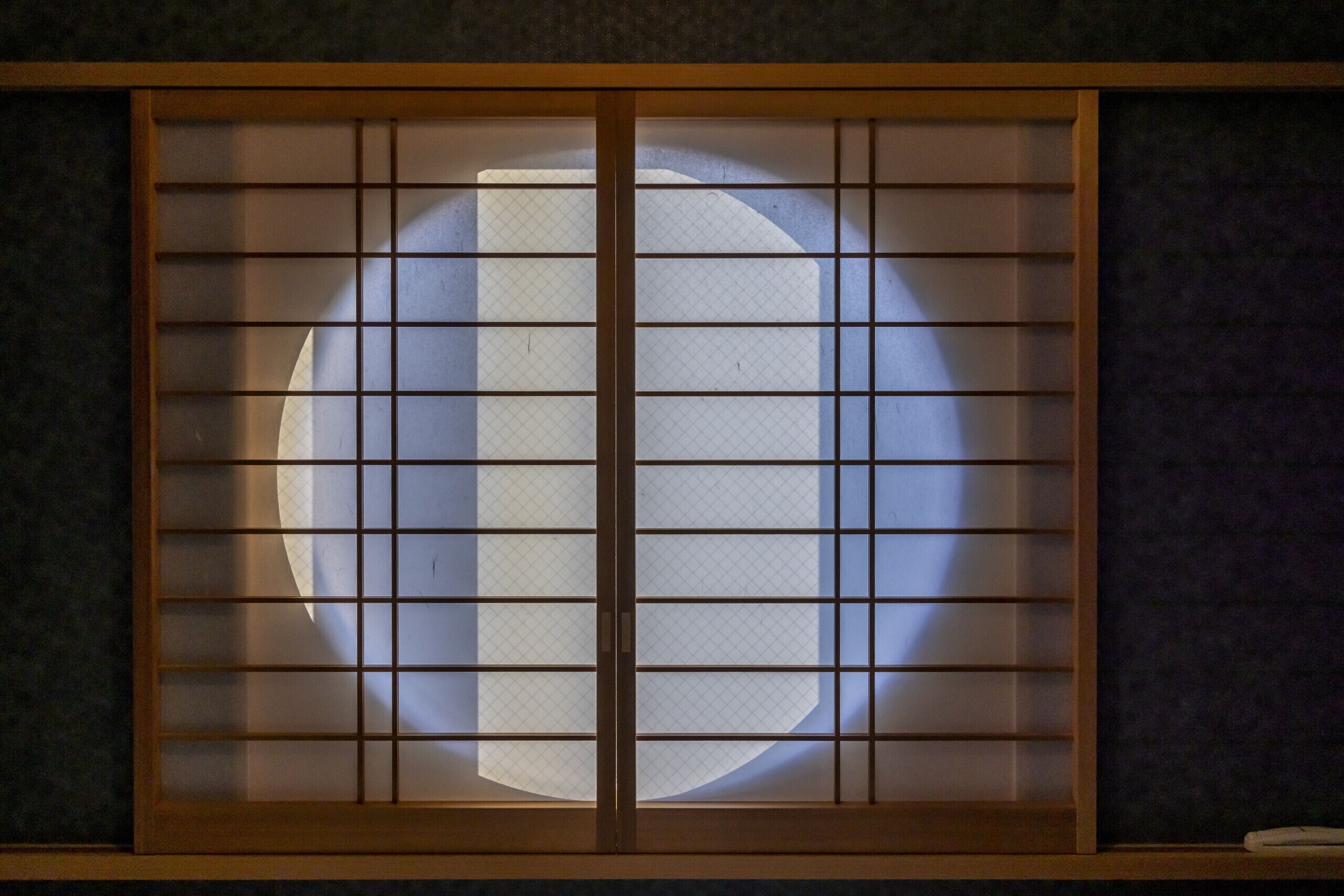 Een traditioneel Japans shoji-scherm met een cirkelvormige uitsparing in het midden, omgeven door houten lattenwerk.