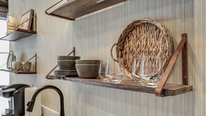A kitchen with a wooden shelf holding bowls, glasses, and a woven basket.