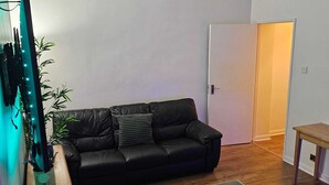 Un salon avec un canapé en cuir noir, une table d’appoint en bois, un tapis gris et une petite table en bois.