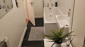Une salle de bain moderne avec une baignoire, une douche et un lavabo. Un miroir est accroché au mur et une plante en pot est posée sur le comptoir.