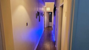 Un couloir doté d’un plancher en bois, de murs blancs et d’un mur d’accent bleu. Des tableaux encadrés ornent le mur, et un luminaire suspendu est fixé au plafond.