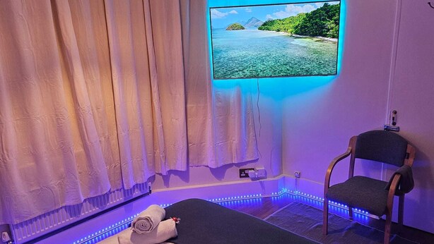 Une pièce comprenant un lit, une chaise, un téléviseur fixé au mur et des éclairages à LED.
