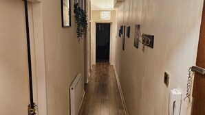 Un couloir étroit avec un radiateur, une plante suspendue et un téléphone fixé au mur.