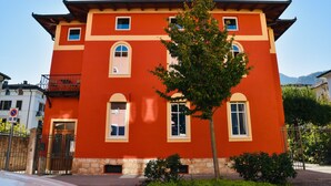 A two-story building with a red facade, multiple windows, and a small tree in front. - Nine Rooms Apartment (Trento)