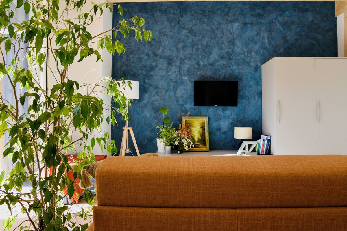 Ein Zimmer mit blauer Wandstruktur, einem angebrachten Fernseher, einer weißen Kommode und einem braunen Sofa.