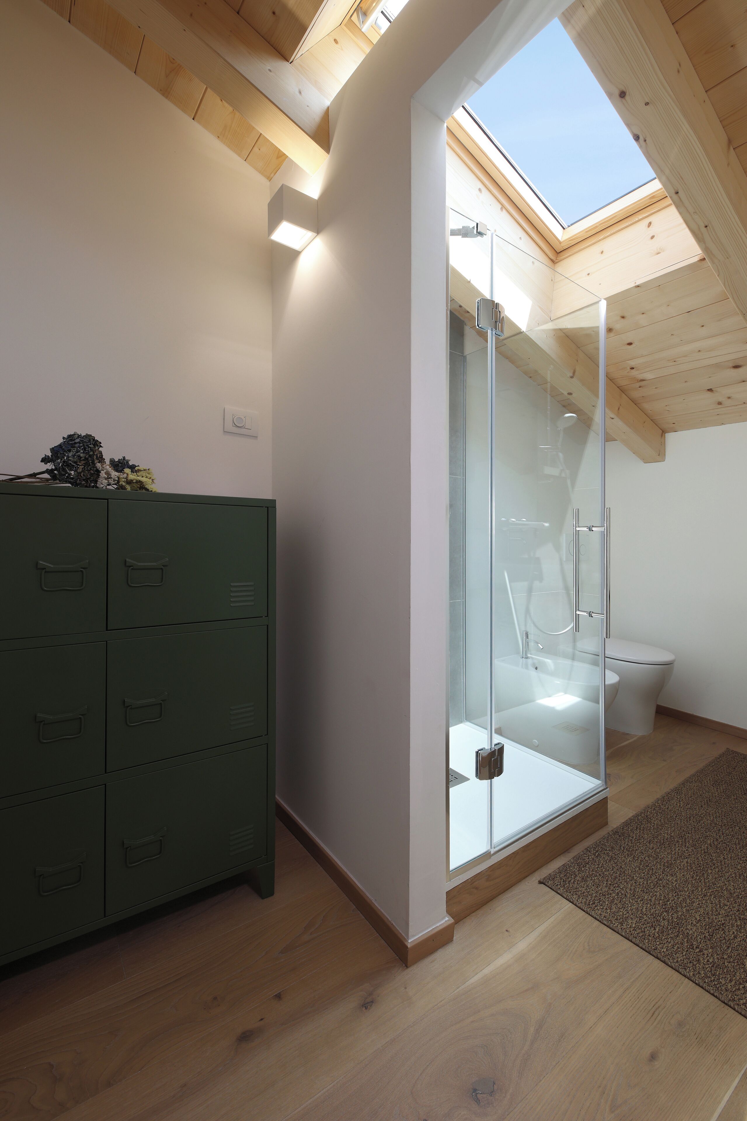 A modern bathroom with a skylight, a glass shower enclosure, and a green storage unit.