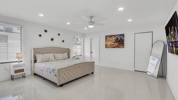 Une chambre à coucher comprenant un lit, un ventilateur de plafond, une table de chevet, une lampe, une porte et un radiateur fixé au mur.
