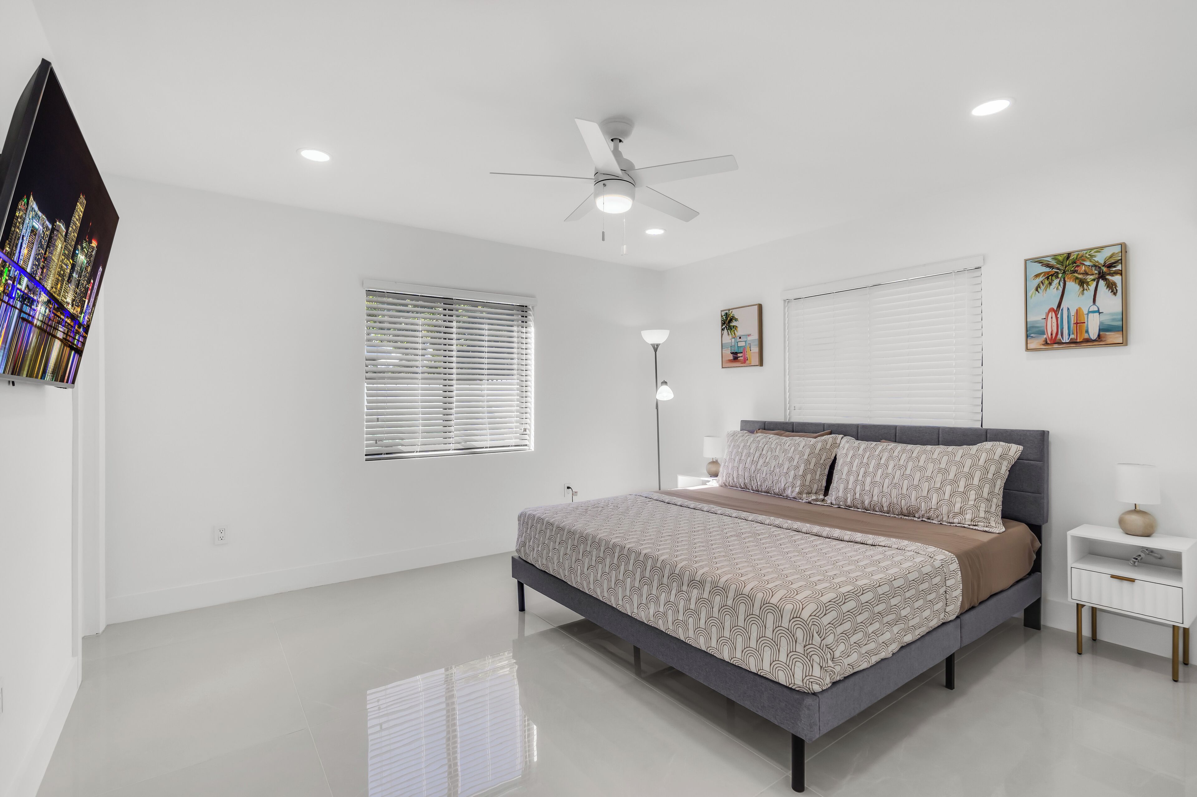 Une chambre à coucher moderne avec un lit, un ventilateur de plafond, une table de chevet et un téléviseur fixé au mur.