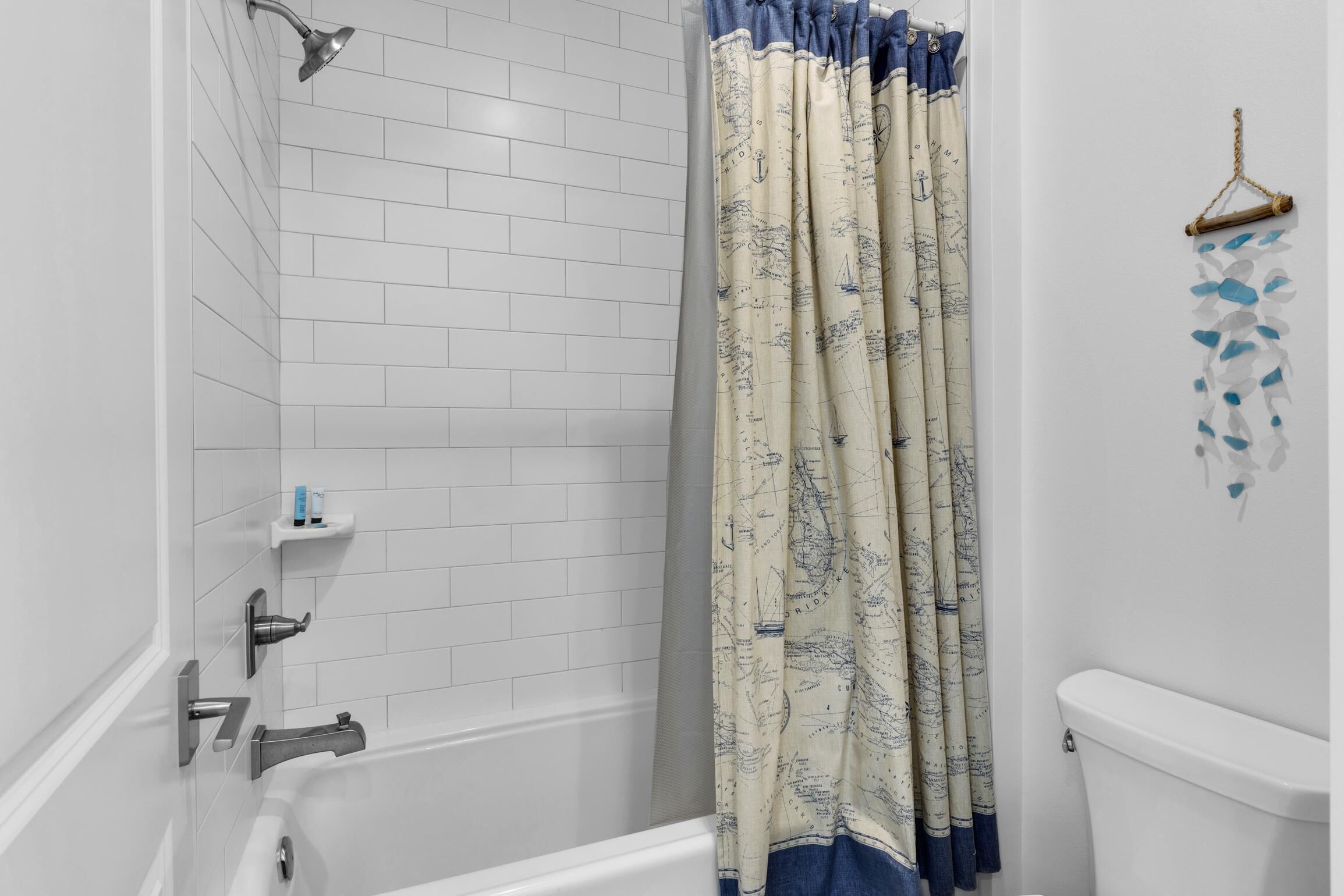 A bathroom with white tiled walls, a bathtub, a showerhead, and a toilet.