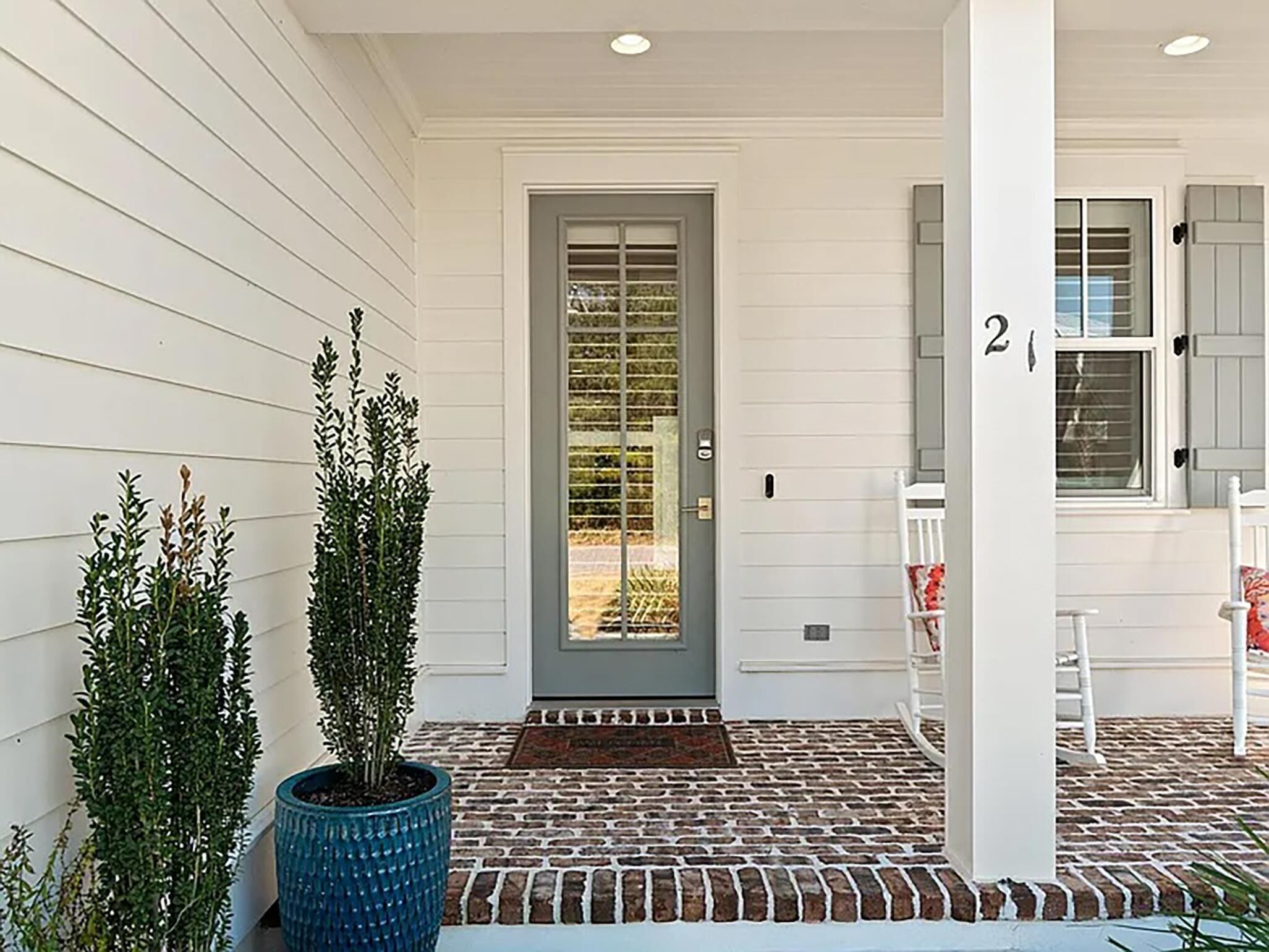 A front porch with a grey door, a brick pathway, and two potted plants.