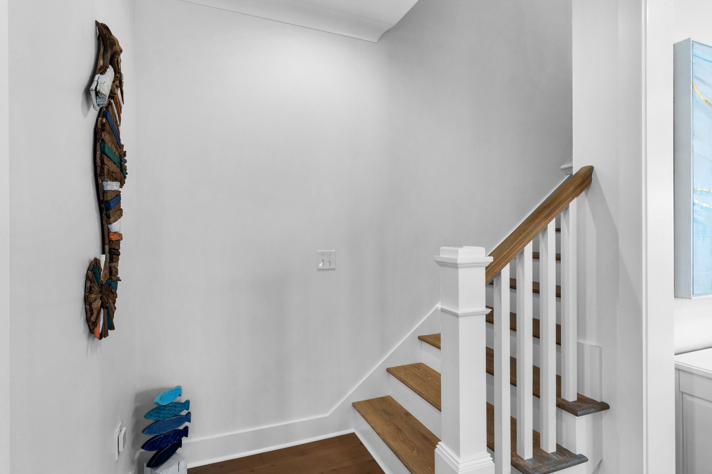 Un escalier avec des marches en bois et des rampes blanches, menant à un palier où est accrochée une œuvre d’art au mur.
