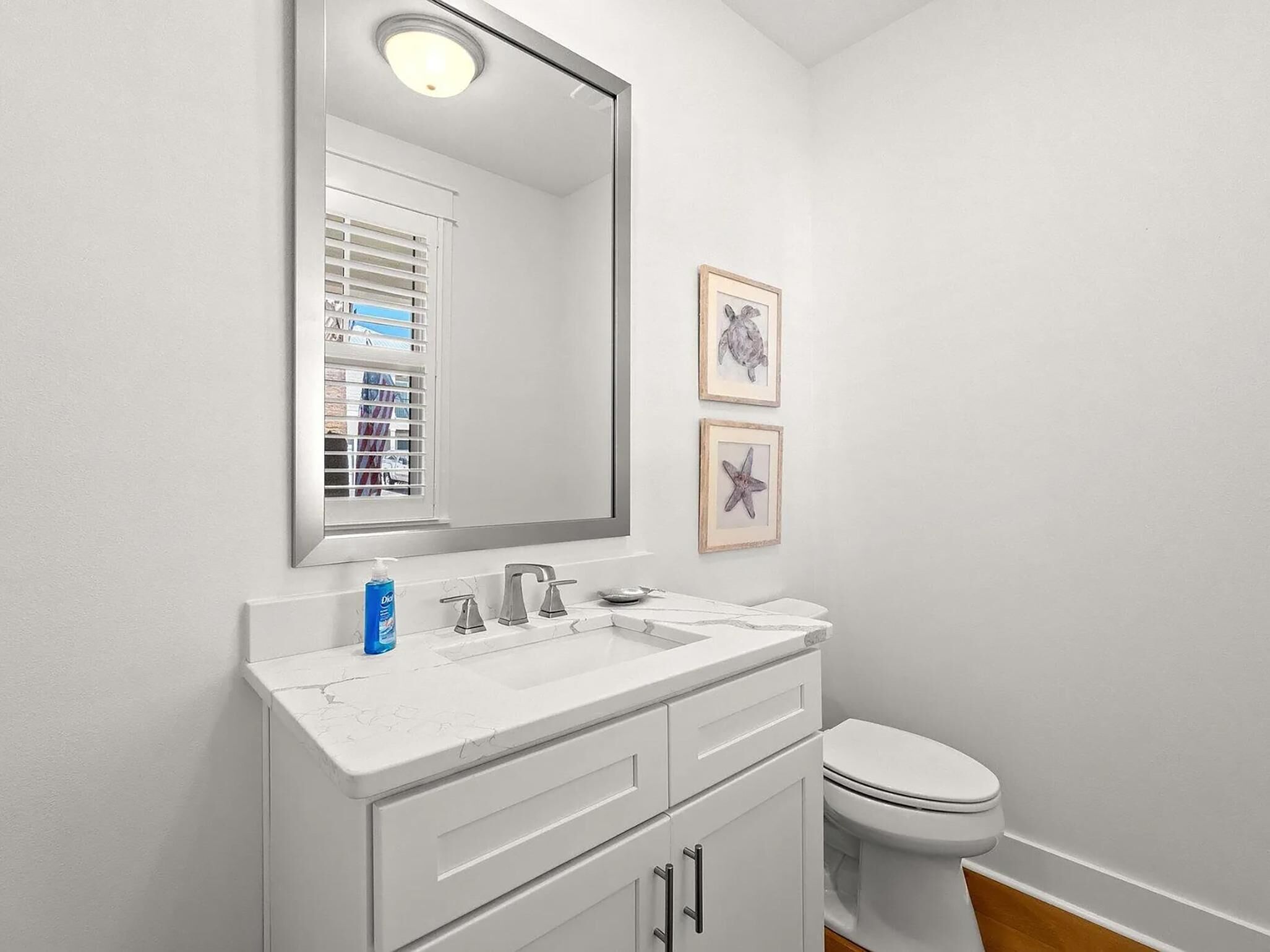Une salle de bain avec un meuble-lavabo blanc, un évier, un miroir et des toilettes. Deux tableaux encadrés sont accrochés au mur.