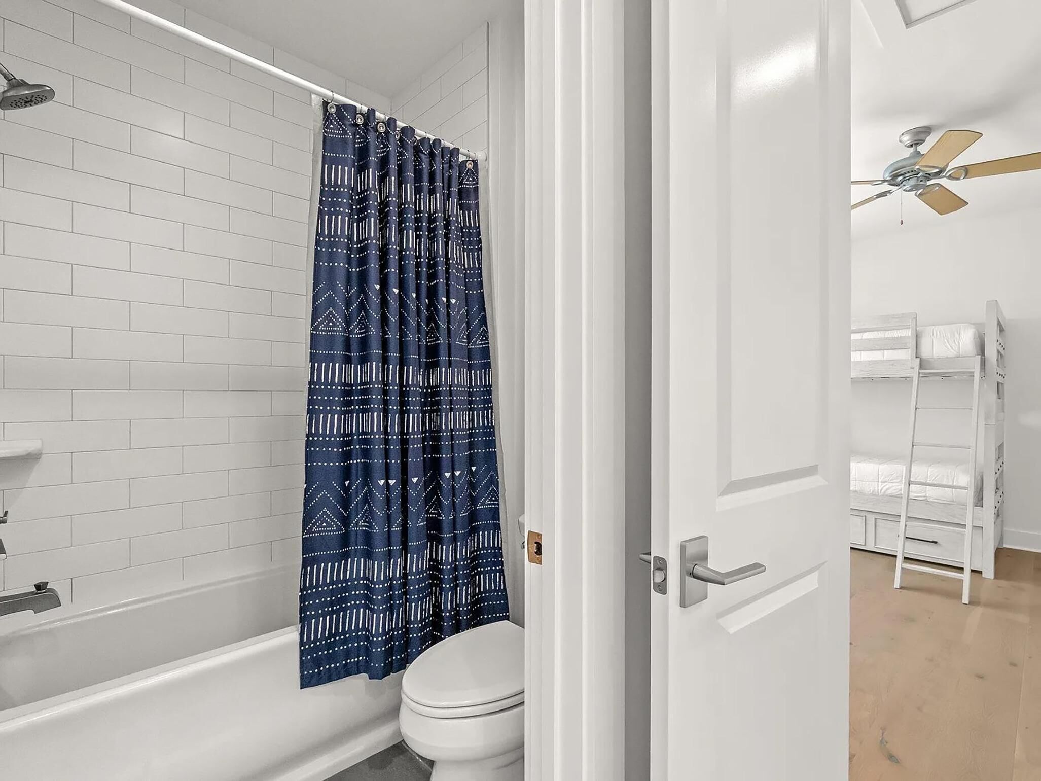 Une salle de bain avec une baignoire blanche, une pomme de douche, des toilettes et un rideau de douche bleu à motifs.